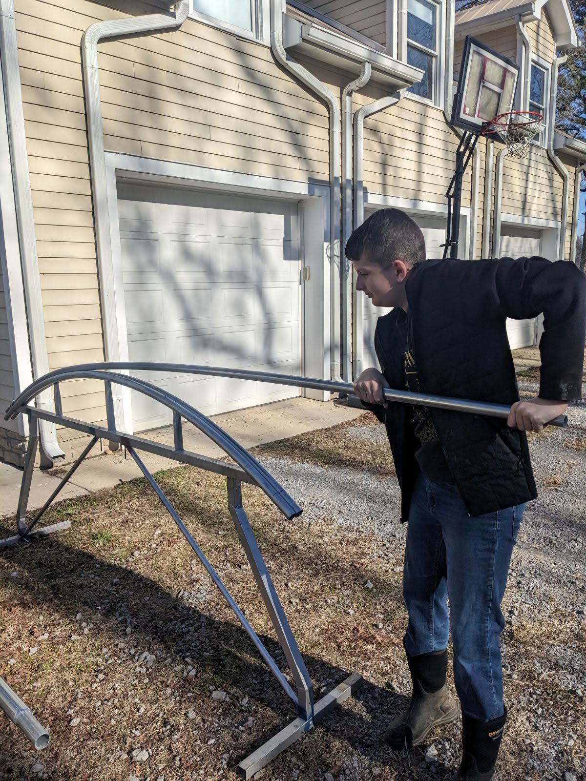 Image showing a young man bending a galvanized steel pipe that will be used as a component in a greenhouse kit. 